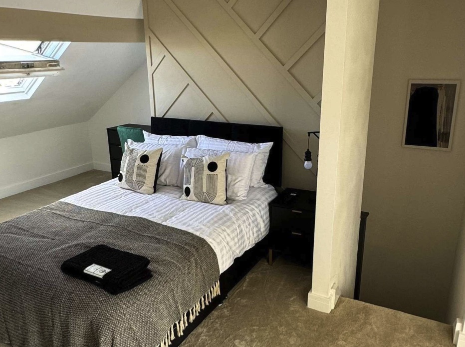 A double bedroom with a cream upholstered feature wall and skylight