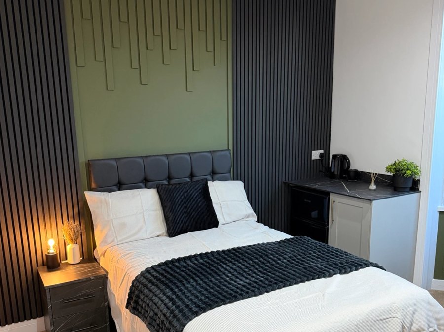 A furnished double bedroom at 8 Station Road, Darlington, with a dark slatted feature wall and bay window